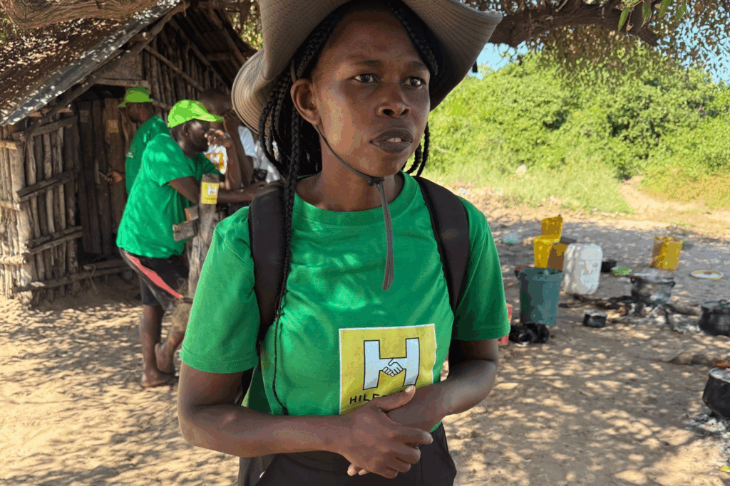 Leiterin eines Klimaprojekts in Mosambik, im Hintergrund zwei Mitarbeiter vor einer Hütte