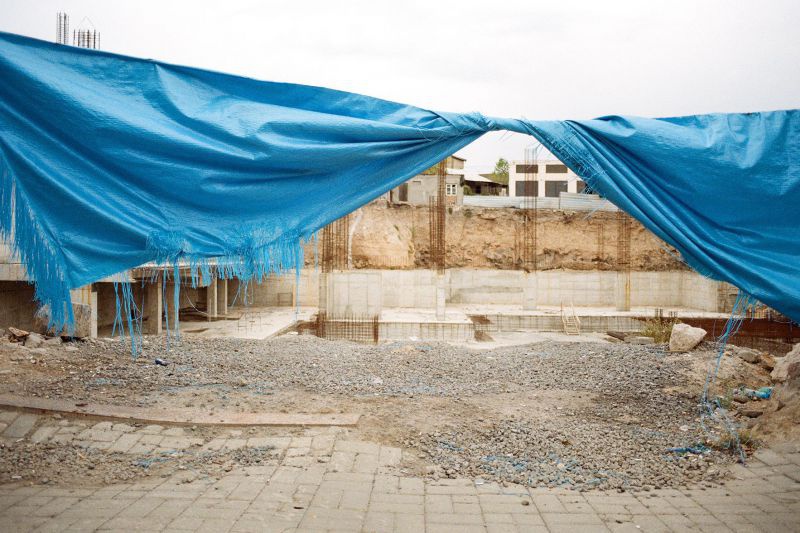 Baustelle, davor eine blaue, zerschlissene Plastikplane